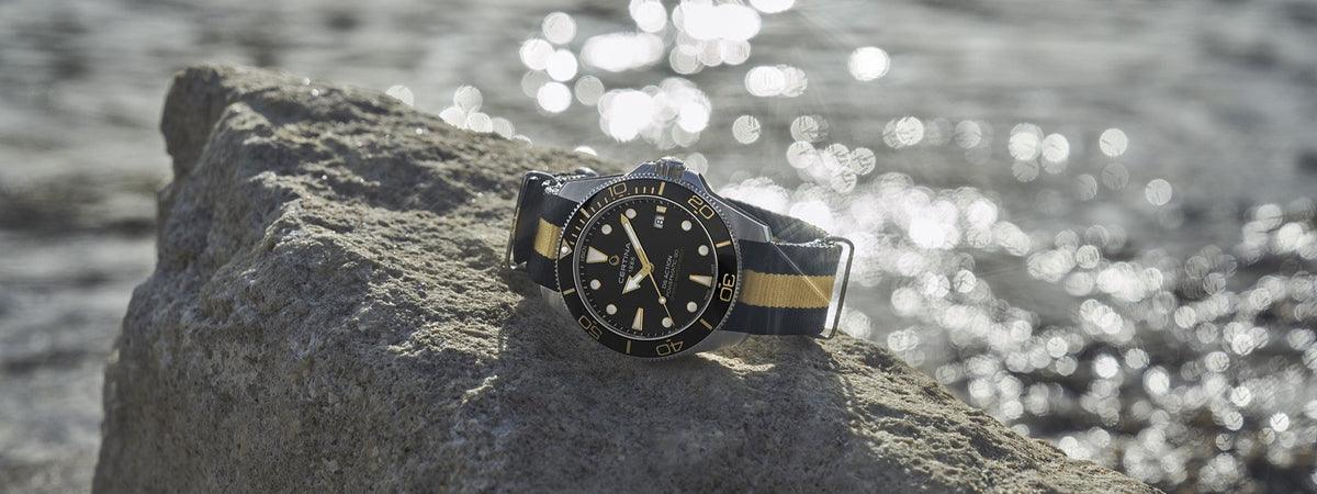 Certina ur der ligger på sten med havet i baggrunden