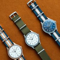 Certina DS Powermatic 80 herreur med blå skive og flerfarvet natorem, set forfra ved siden af andre ure