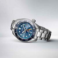 Seiko herreur i stål med blå urskive med orange GMT-viser og blå krans. Uret ses liggende på et bord.