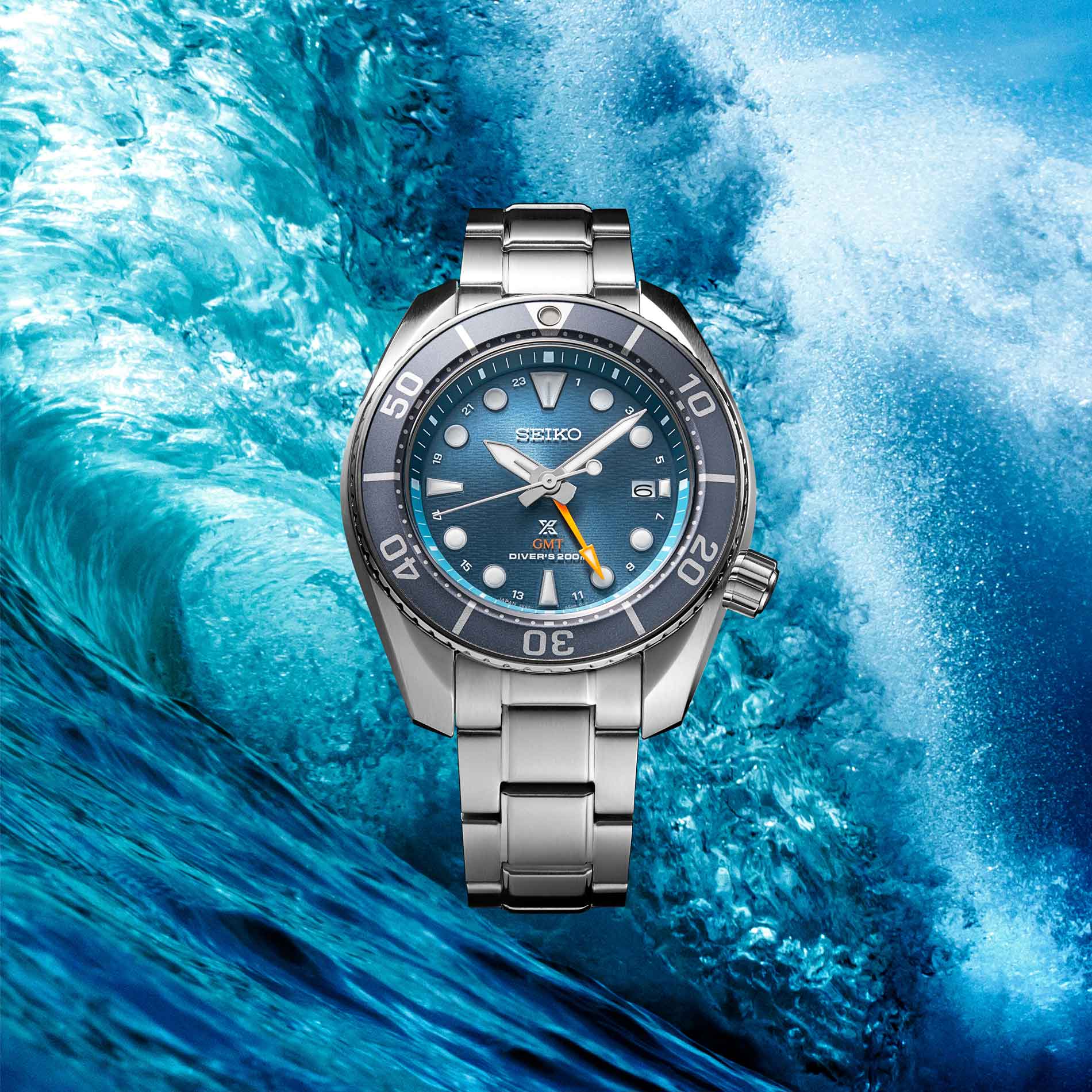 Seiko herreur i stål med blå urskive med orange GMT-viser og blå krans. Uret ses på en baggrund af vand og bølger.