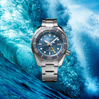 Seiko herreur i stål med blå urskive med orange GMT-viser og blå krans. Uret ses på en baggrund af vand og bølger.