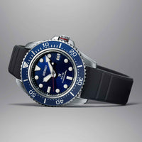 Seiko herreur i stål med blå urskive og blå krans. Uret har en sort solikonerem. Uret ses liggende på en grå baggrund.