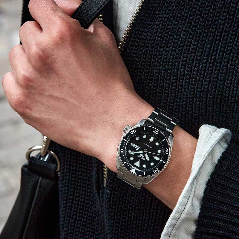 Seiko herreur i stål med sort urskive. Uret ses på et håndled.