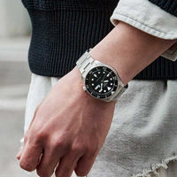 Seiko herreur i stål med sort urskive. Uret ses på et håndled.