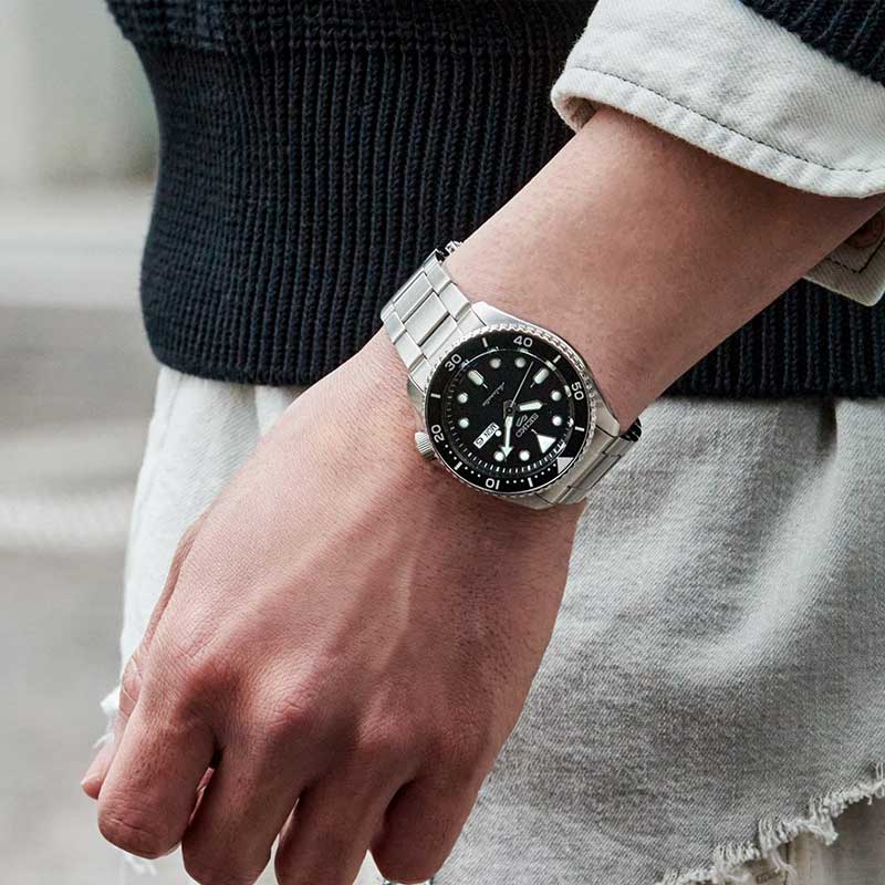 Seiko herreur i stål med sort urskive. Uret ses på et håndled.