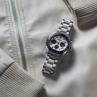 Seiko herreur i stål med hvid urskive med tre sorte chronographer. Uret ses liggende på en hvid jakke.