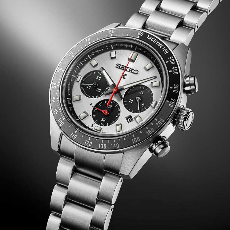 Seiko herreur i stål med hvid urskive med tre sorte chronographer. Uret har også sort urkrans. Uret ses skråt forfra med åben lænke på sort baggrund.