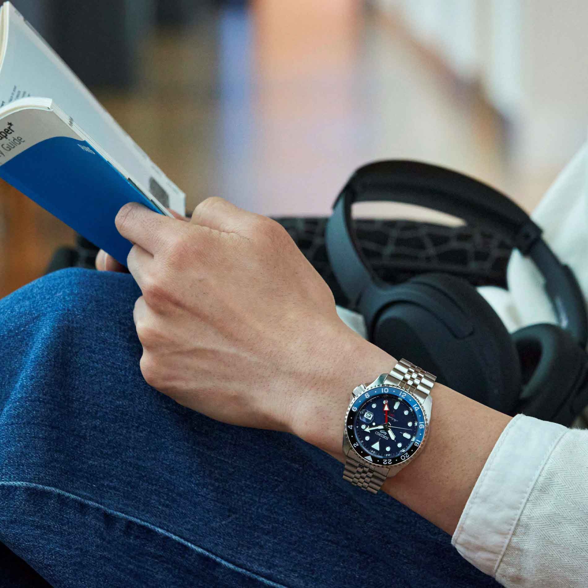 Seiko herreur i stål med blå urskive, hvide visere og indekseringer samt rød GMT-viser. Uret ses på et håndled.