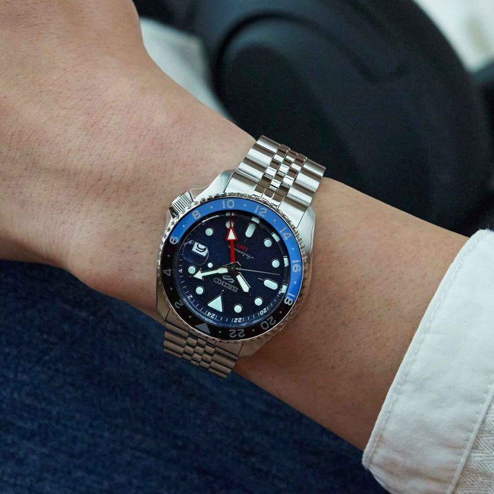 Seiko herreur i stål med blå urskive, hvide visere og indekseringer samt rød GMT-viser. Uret ses på et håndled.