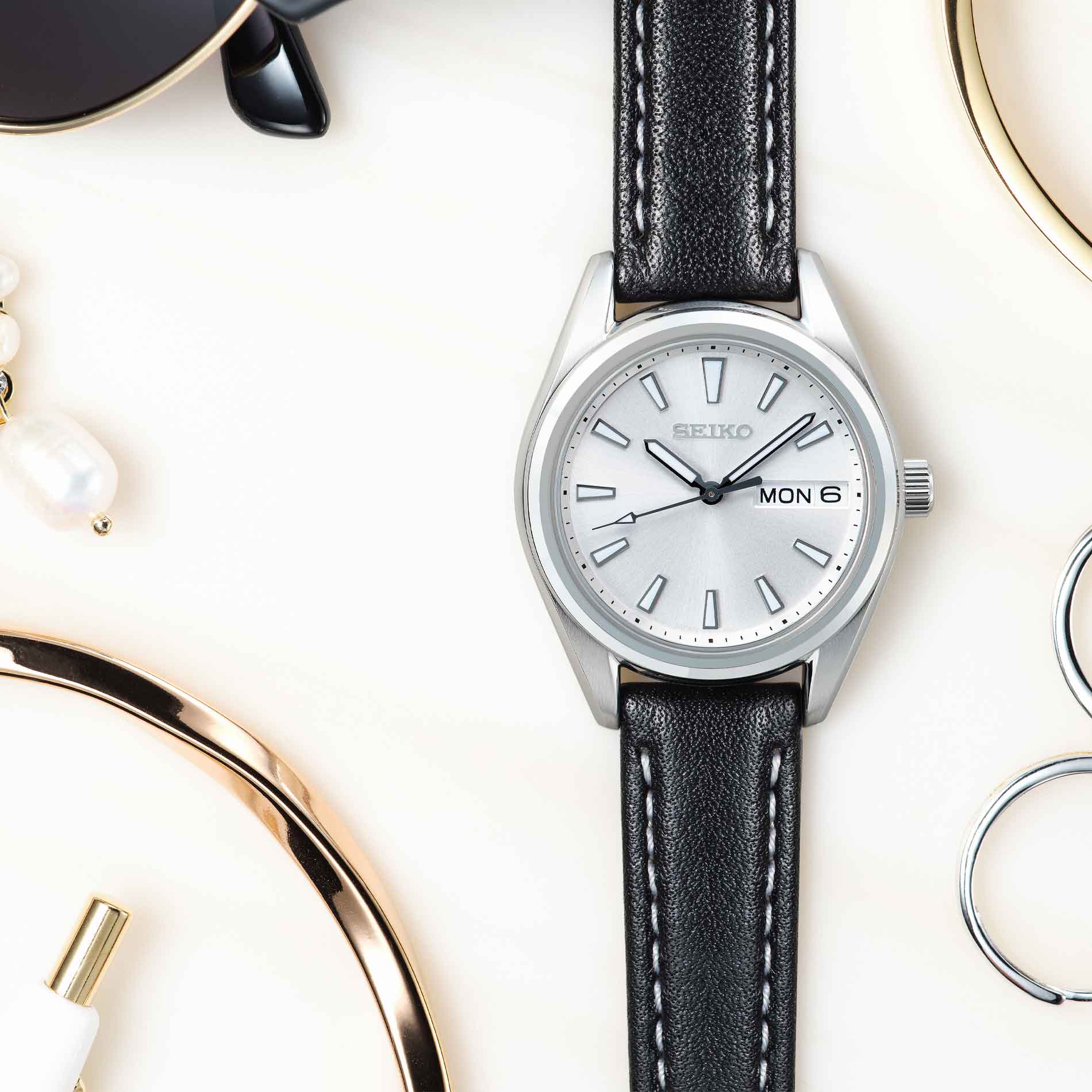 Seiko dameur i stål med sort læderrem. Uret ses liggende på hvidt underlag.