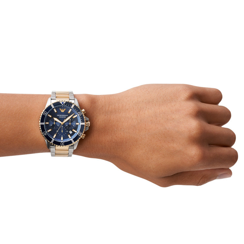 Emporio Armani Diver AR11362 herreur med en stål-urkasse og stållænke. Uret har gyldne detaljer på kasse og lænke samt en sort urskive og datovisning. Uret ses på håndledet af en mand.