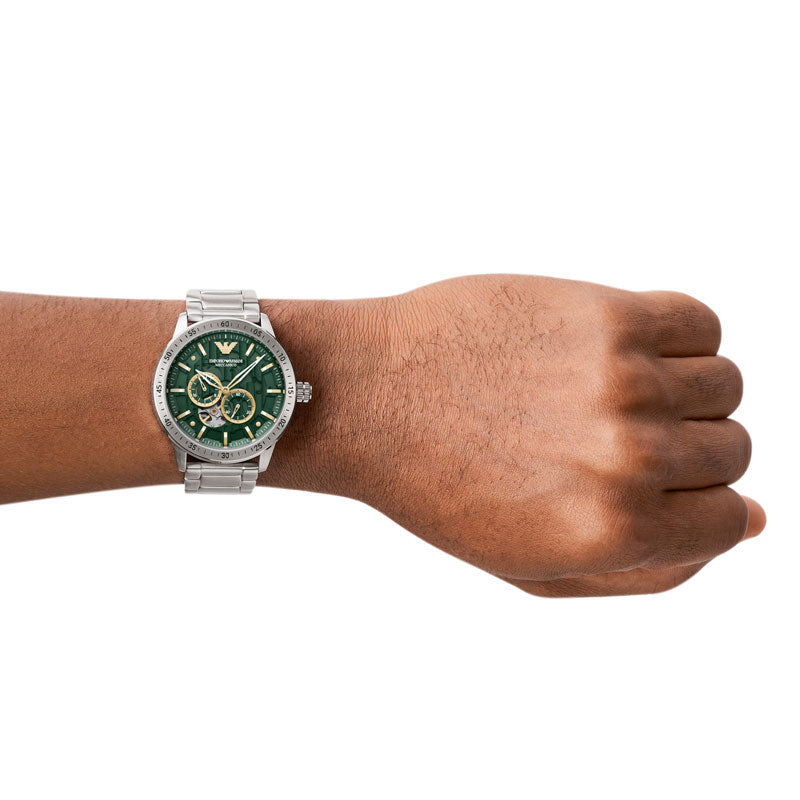 Emporio Armani Mario AR60053 automatisk herreur i stål med lænke og transparent bagkasse. Uret har en grøn skive med gulddetaljer. Uret ses på håndledet af en mand.