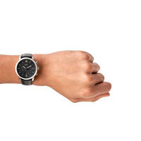 Fossil Neutra Chrono herreur i stål med sort urskive og sort læderrem. Uret ses på håndledet af en mand.