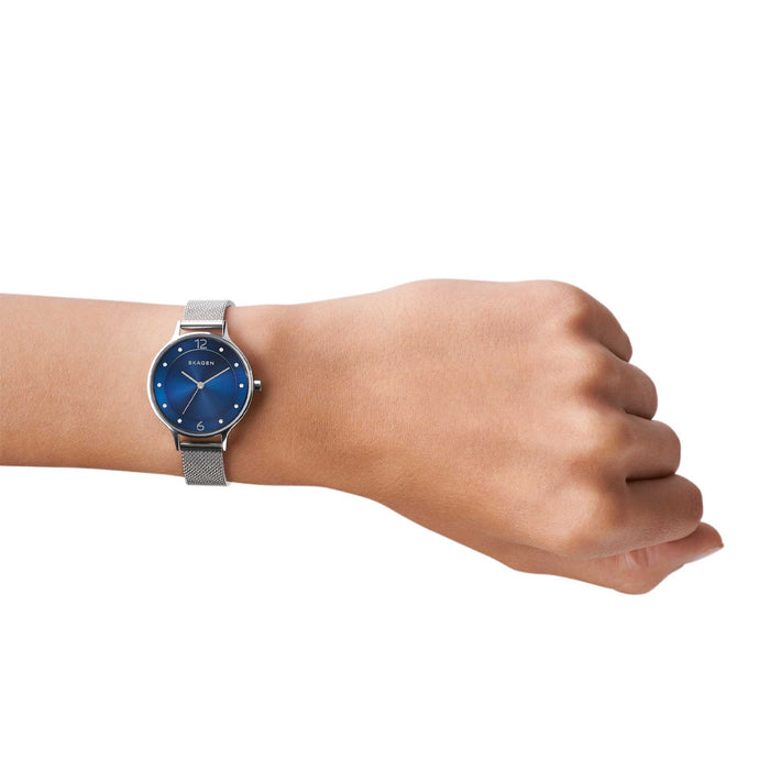 Skagen dameur i rustfrit stål med meshlænke, blå urskive og funklende sten. Uret ses på et håndled.