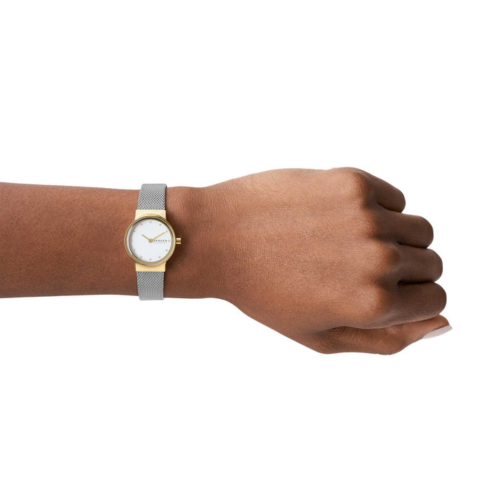 Skagen dameur i stål med meshlænke, funklende sten og guldfarvet urkasse. Uret ses på et håndled.