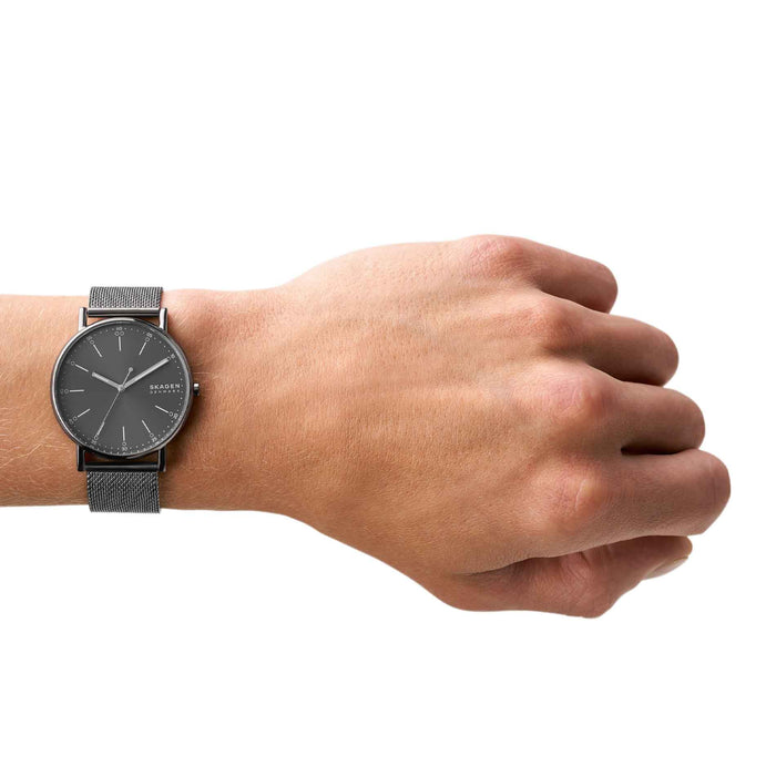 Skagen herreur med grå stålurkasse, grå skive og grå meshlænke. Uret ses på et håndled.