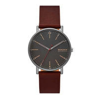 Skagen ur med stålurkasse, sort skive og brun læderrem. Uret har arabertal på skiven. Uret ses forfra.