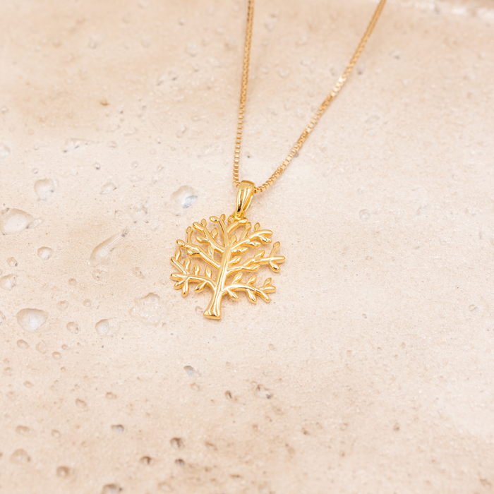 Forgyldt sølv halskæde med træformet vedhæng liggende på lys stenoverflade