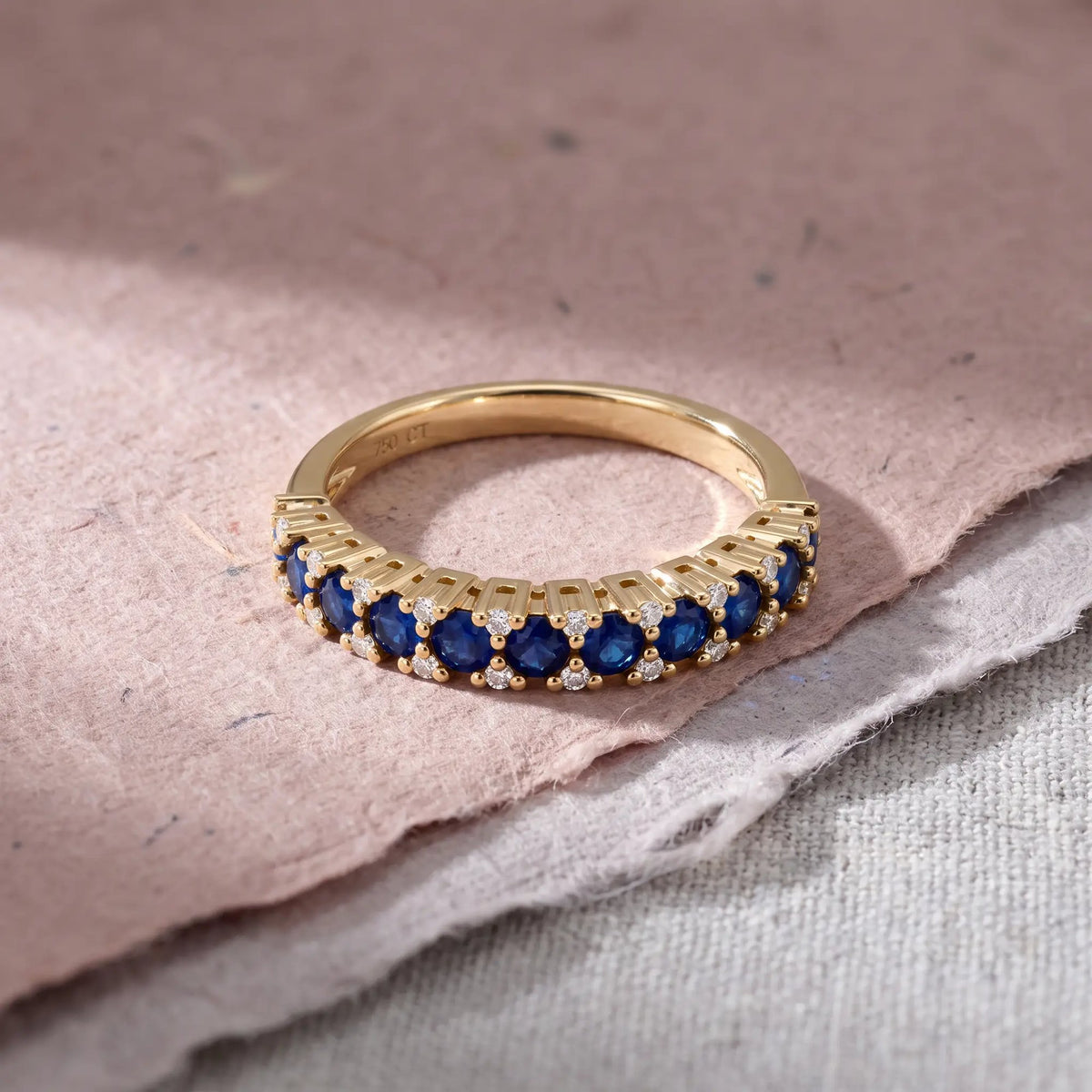 Adeline ring i guld med blå safirer og diamanter på lyserødt papir