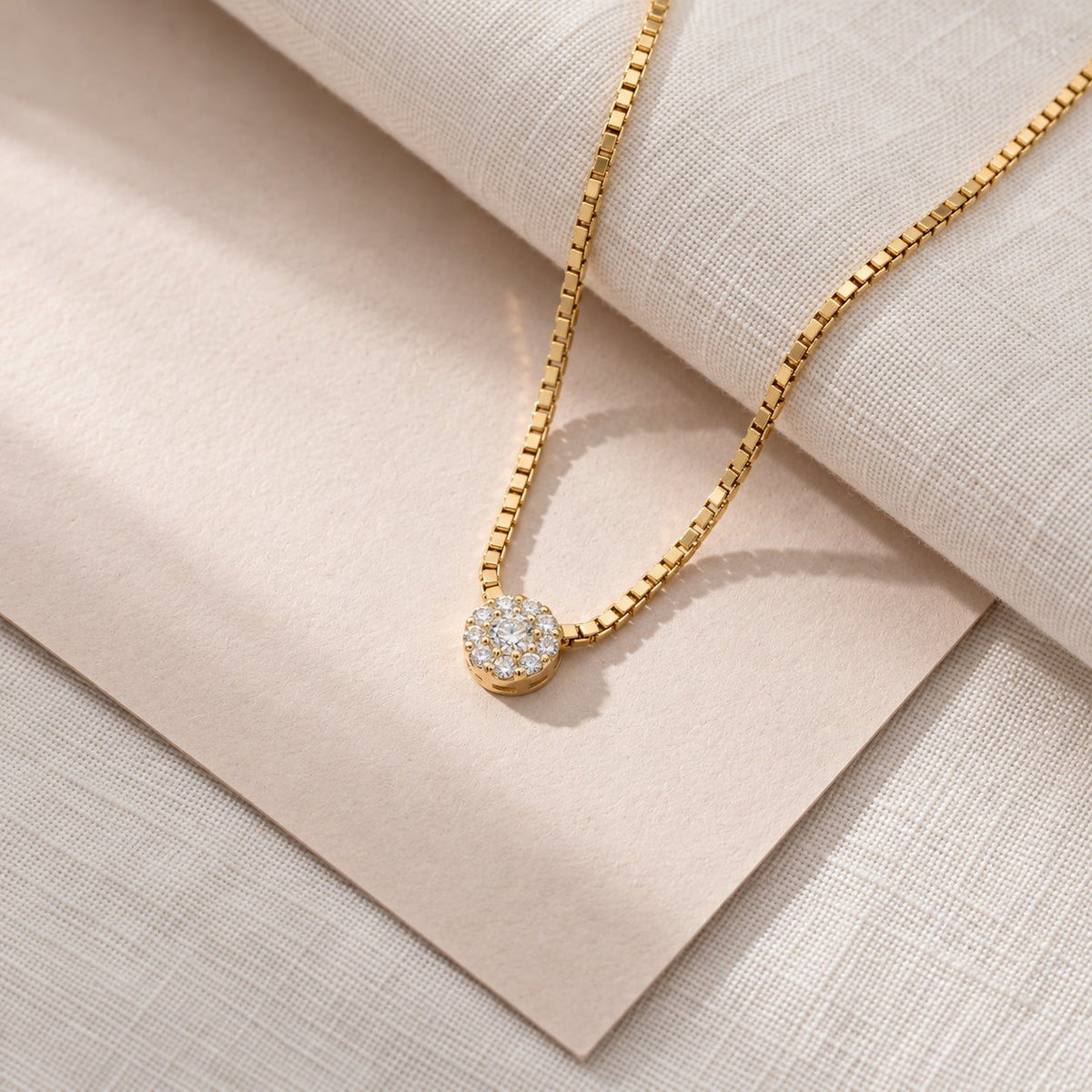 Alma vedhæng i guld med 0,16 carat diamanter på venetianerkæde over lyst stof