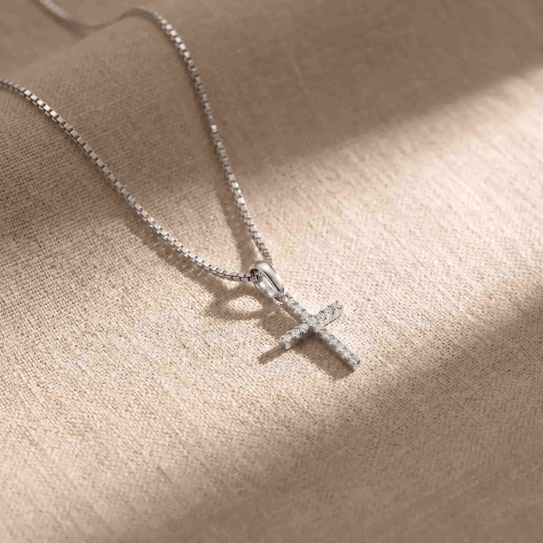 Diamond Cross vedhæng i 18 karat hvidguld med 0,08 carat hvide diamanter, fotograferet på beige stof