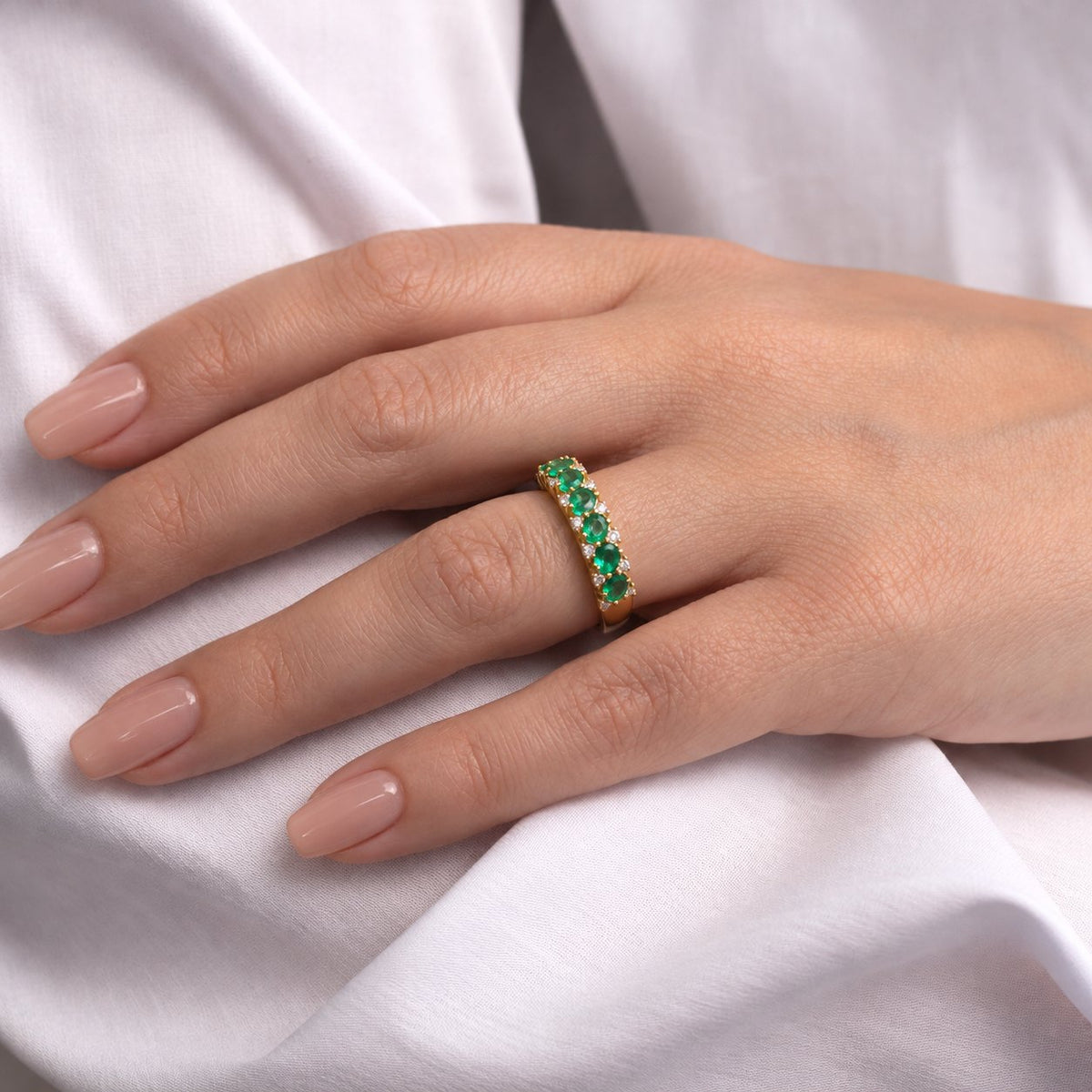 Kvinde i hvid skjorte bærer Ebba ring i guld med smaragder