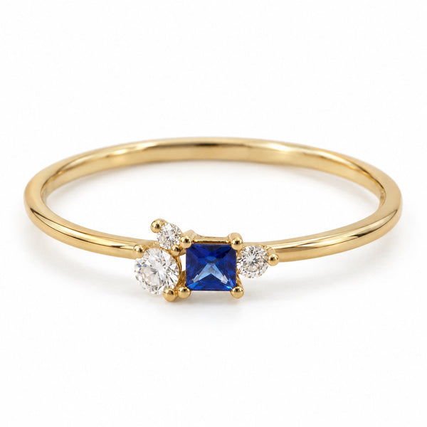 Estelle ring i 18 karat guld med princess-cut blå safir og tre diamanter, hvid baggrund