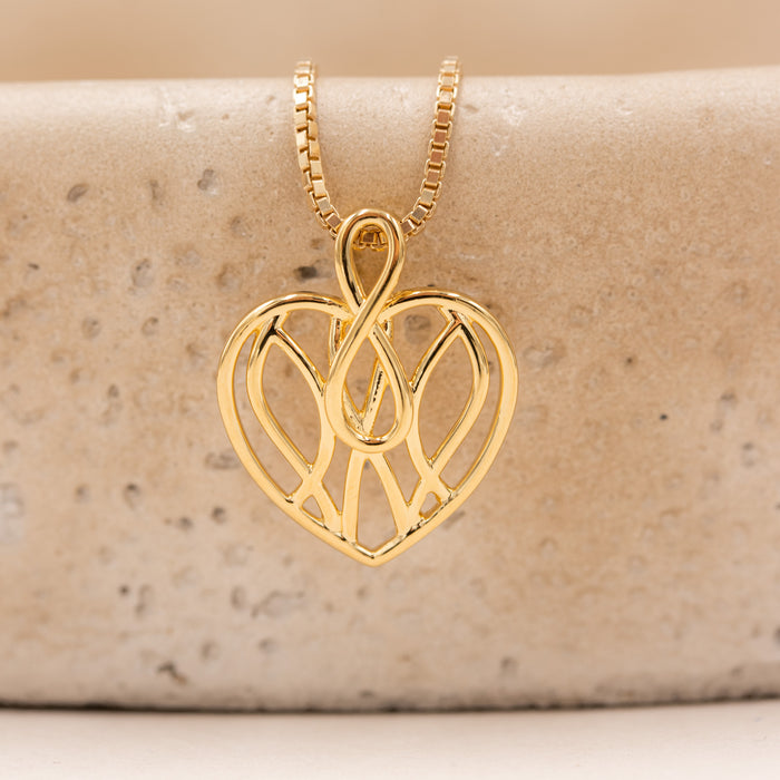 Forgyldt evighedshjerte vedhæng med sammenflettede linjer fotograferet i miljø
