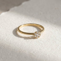 Fleur ring i 18 karat guld med 0,15 carat hvide diamanter, vist på en lys overflade med blødt lys.