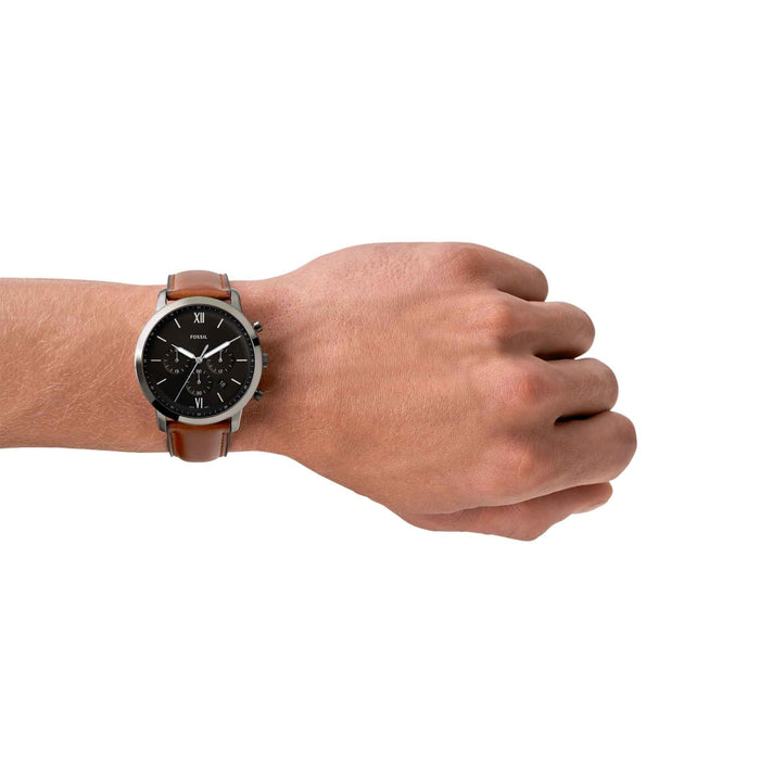 Fossil Neutra Chrono herreur i gunmetal stål med sort urskive og brun læderrem. Uret ses på håndledet af en mand.