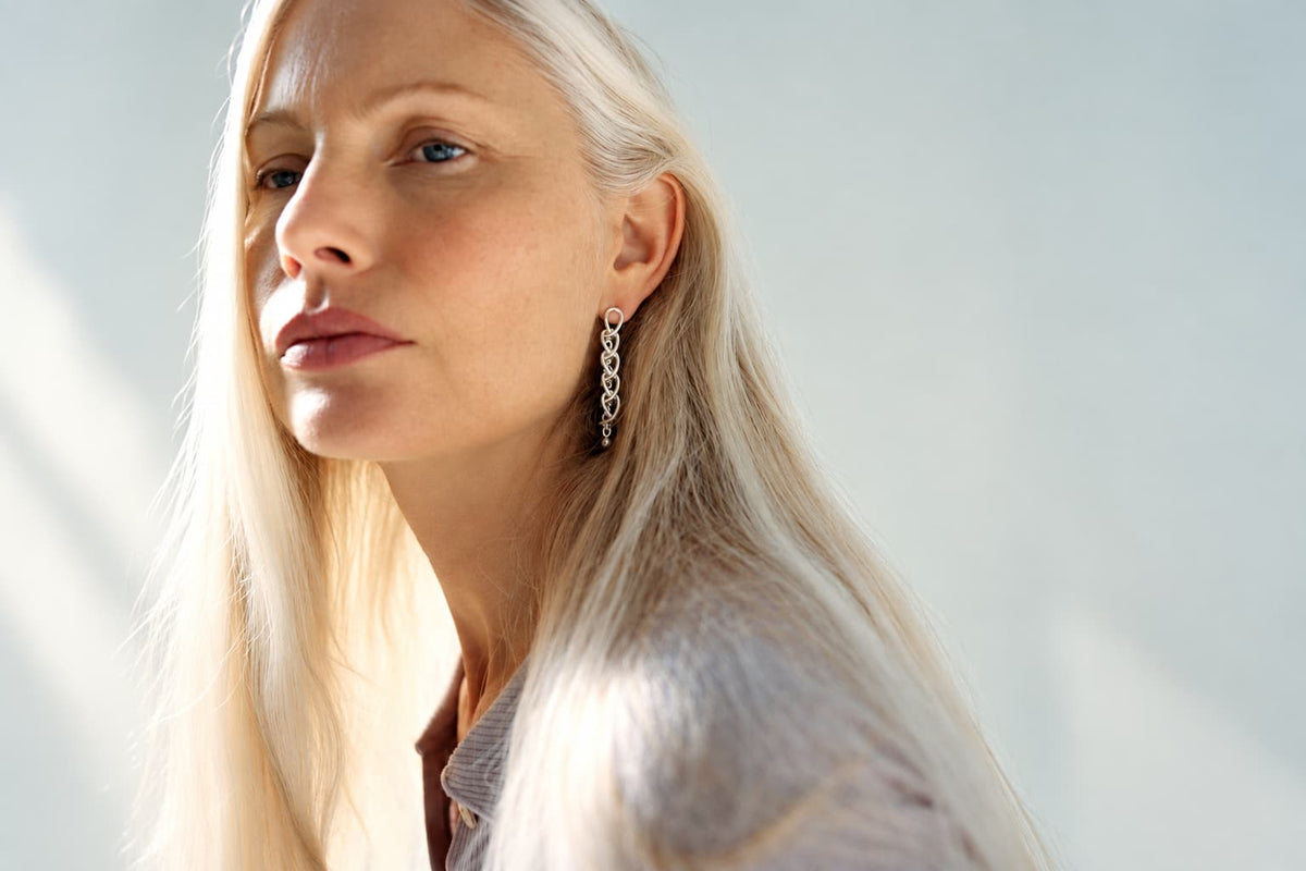 Kvinde med langt lyst hår bærer lange ørehængere i sølv formet som en kæde fra Georg Jensen