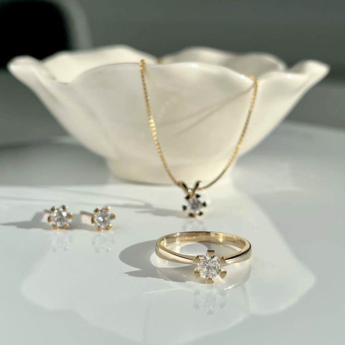 Solitaire diamantring i 8 karat guld med 0,25 carat diamanter, på bord med andre smykker