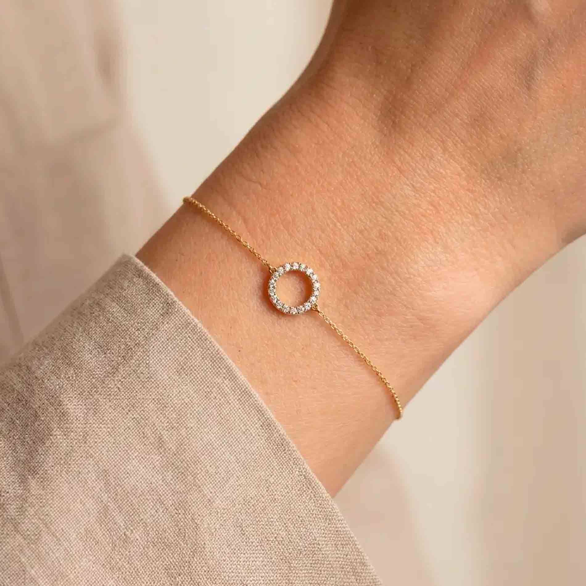 Halo armbånd i 18 karat guld med hvide diamanter vist på et håndled.
