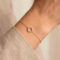 Halo armbånd i 18 karat guld med hvide diamanter vist på et håndled.