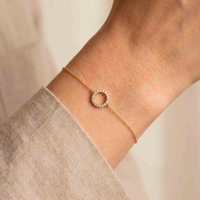 Halo armbånd i 18 karat guld med hvide diamanter vist på et håndled.