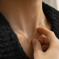 Lilo halskæde med hjertevedhæng i 14 kt. guld med diamanter vist tæt på halsen med hånd ved vedhænget