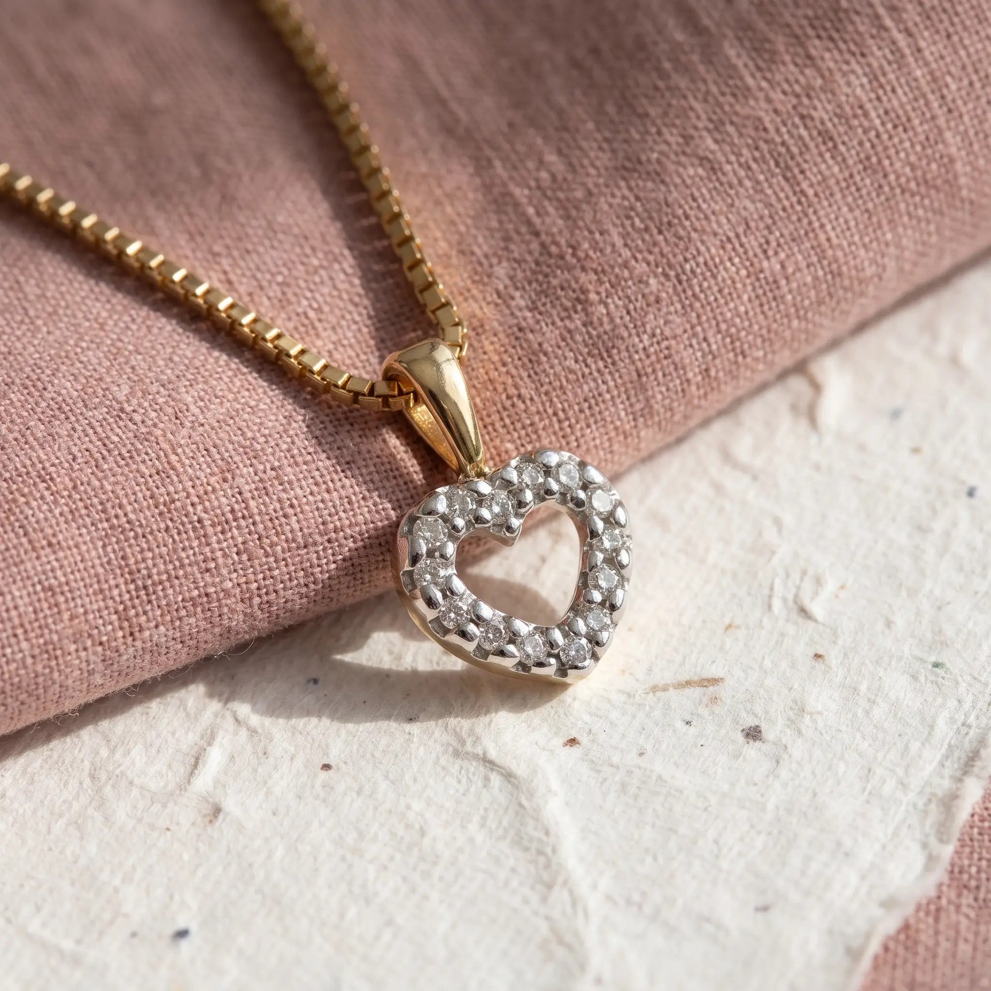 Lilo hjertevedhæng i 14 kt. guld med diamanter på kæde, lagt på rosa stof og hvidt papir