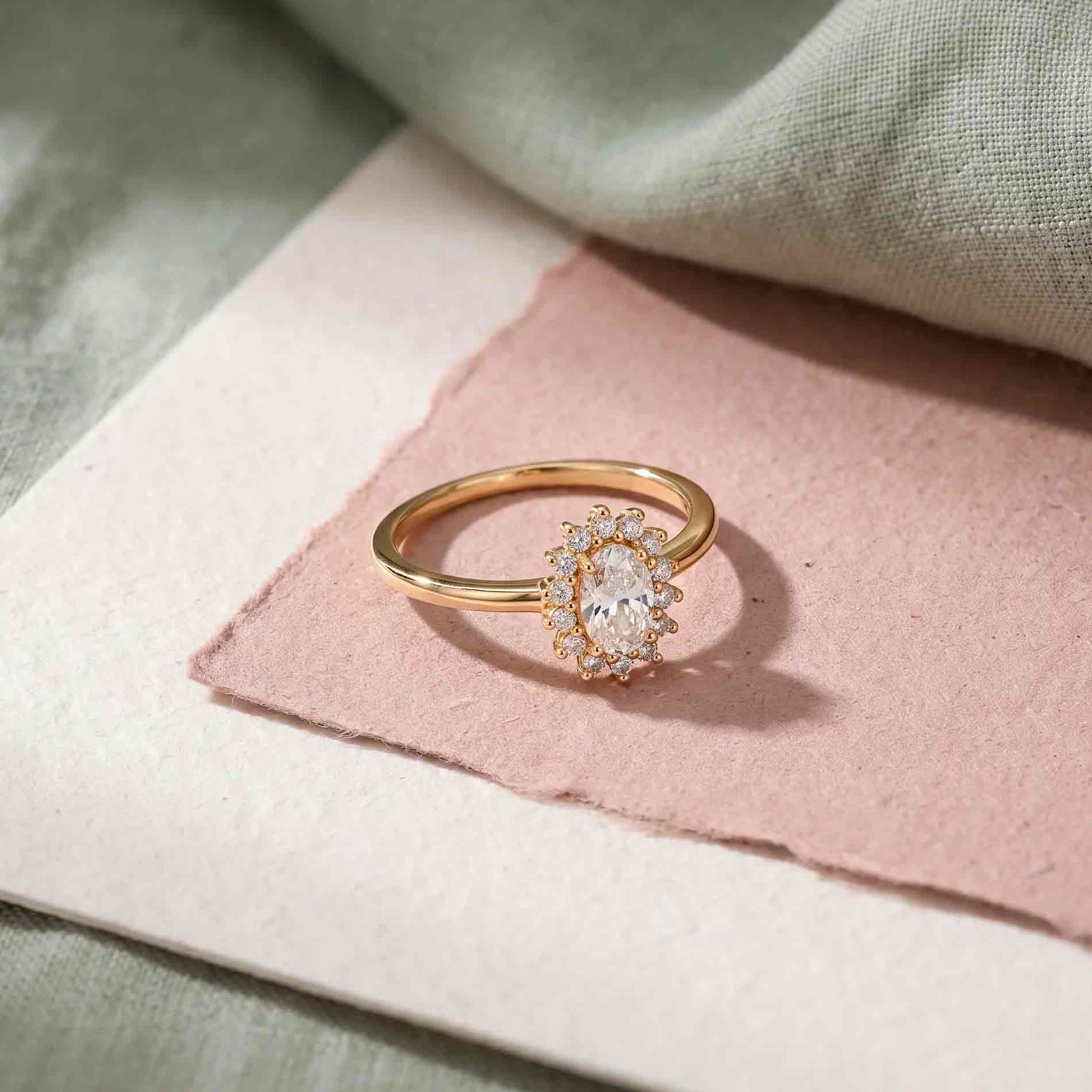 Luda ring i forgyldt sølv med oval klar zirkonia og mindre zirkonia sten på rosa baggrund