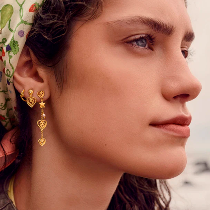 Model bærer Maanesten Sada øreringe i forgyldt sterlingsølv med hvide zirkonia og dekorative hjerter.