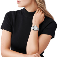 Sølvfarvet Michael Kors Bradshaw MK5739 dameur med romertal og chronograph på en grå urskive. Uret er med sølvfarvet lænke. Uret ses på håndledet af en kvinde iført en sort T-shirt.