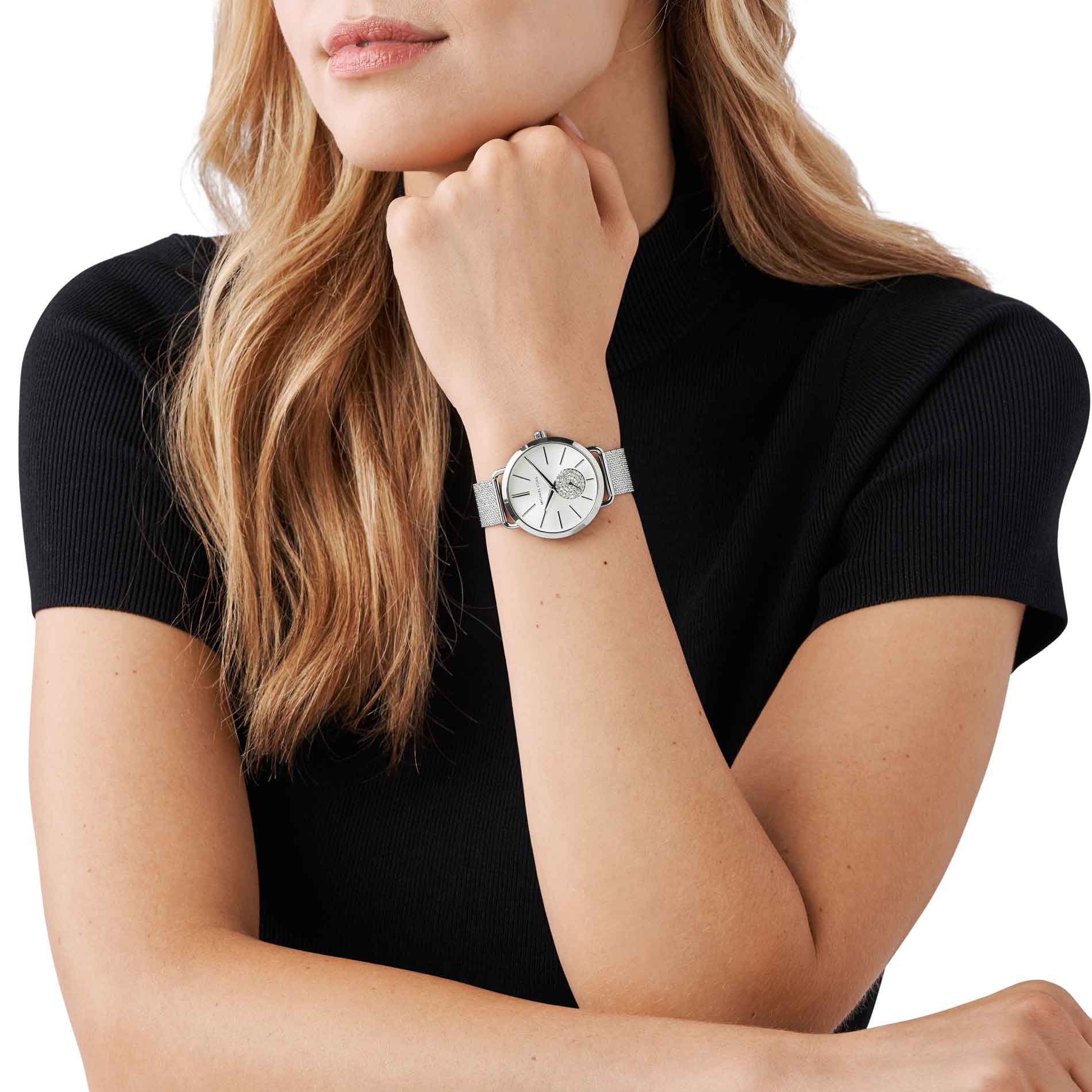 Sølvfarvet Michael Kors Portia MK3843 dameur med hvide sten på chronographen på den grå urskive. Uret har mesh-lænke. Uret ses på håndledet af en kvinde iført en sort T-shirt.