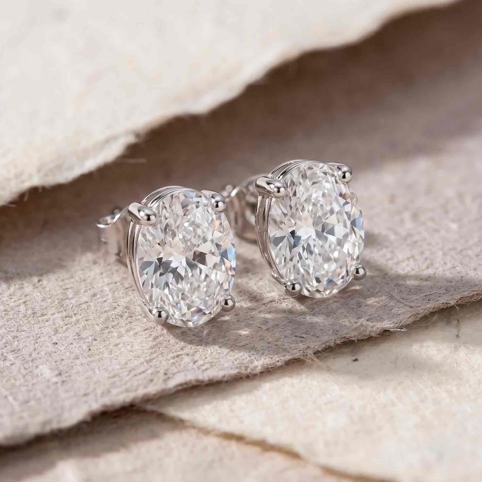Oval-cut VIII Solitaire ørestikker i 925 sterlingsølv med klar zirkonia, vist som elegante sølvørestikker på stof