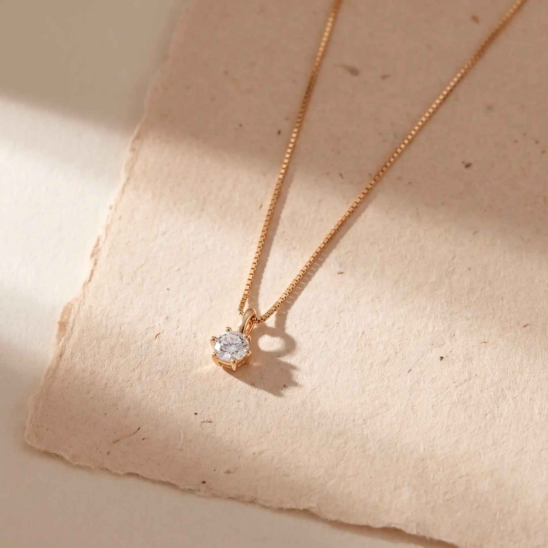 Solitaire vedhæng i 8 karat guld med 7 mm klar zirkonia, vist på lyst stof