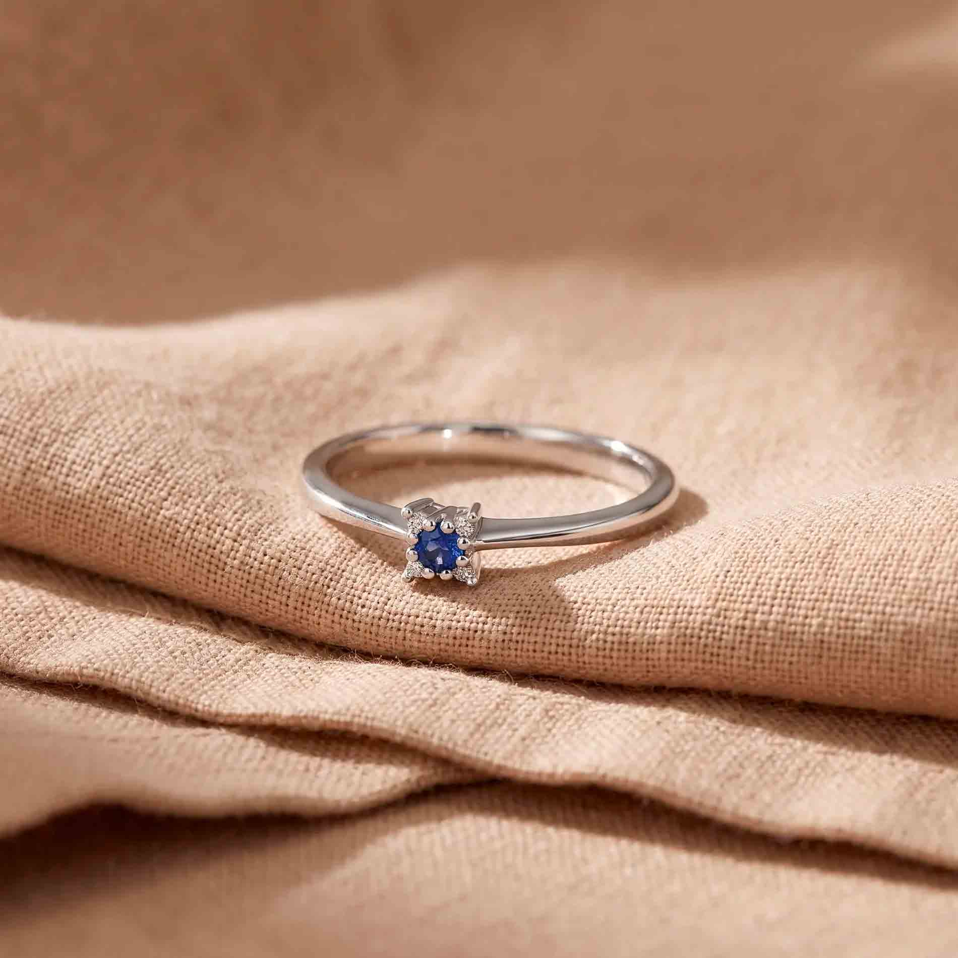 Wilma ring i 18 karat hvidguld med blå safir og diamanter, fotograferet på stof